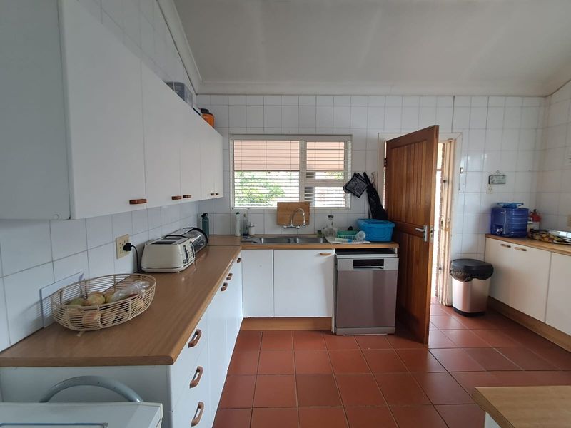 A functional kitchen featuring white cabinetry, laminate countertops, tiled backsplash, and terracotta floor tiles with direct access to the exterior.