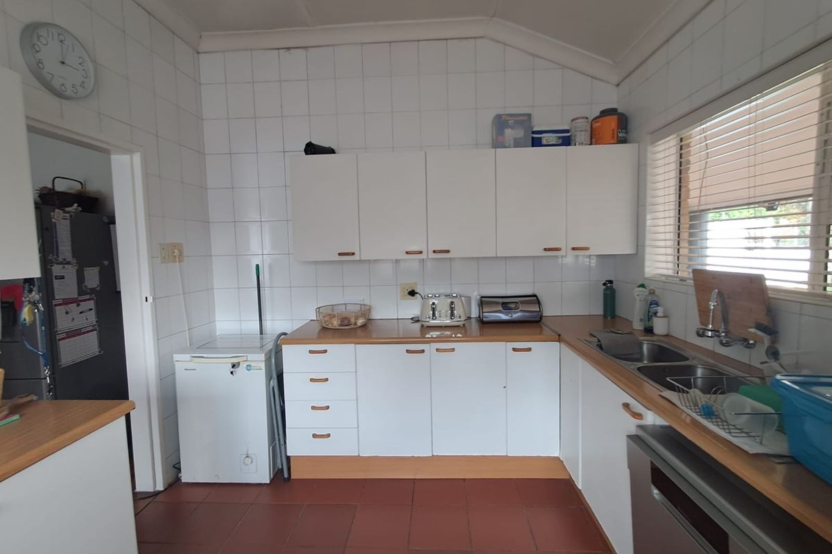 A functional kitchen featuring white cabinetry, laminate countertops, a double bowl sink, and tiled splashbacks with terracotta-style floor tiles.