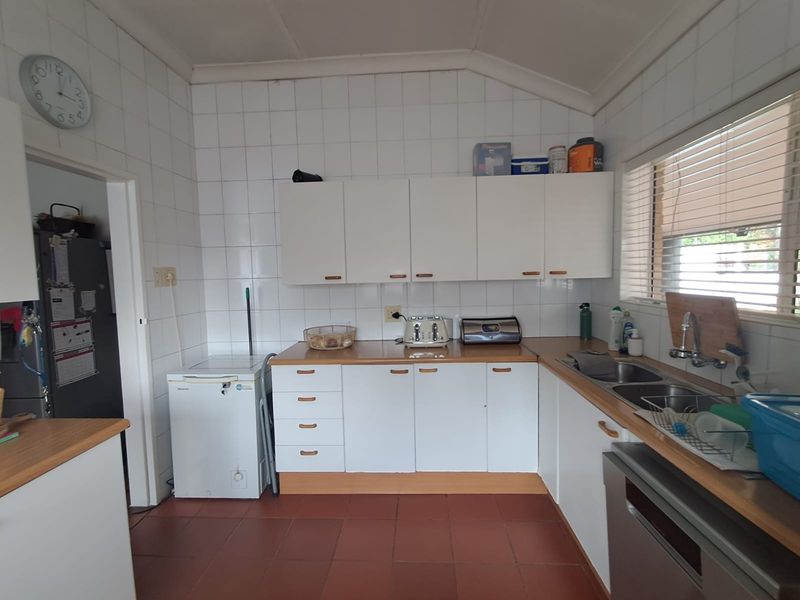 A functional kitchen featuring white cabinetry, laminate countertops, a double bowl sink, and tiled splashbacks with terracotta-style floor tiles.