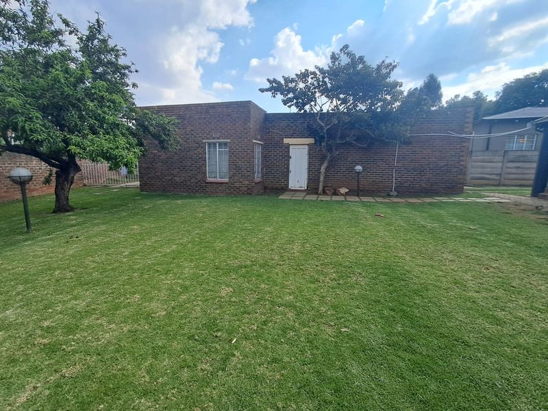 A view of the rear exterior of the house featuring a brick facade, security bars on windows, and a well-maintained lawn.