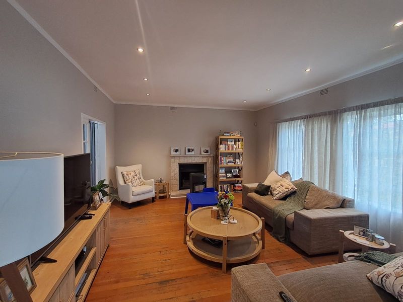 A spacious living room featuring warm timber flooring, a central fireplace, and recessed downlighting, creating a comfortable and inviting atmosphere.