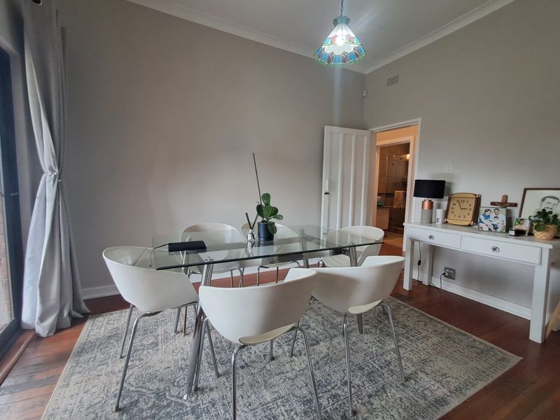 A well-lit dining room featuring hardwood flooring, coved cornicing, and a decorative stained glass pendant light, providing a comfortable space for meals.