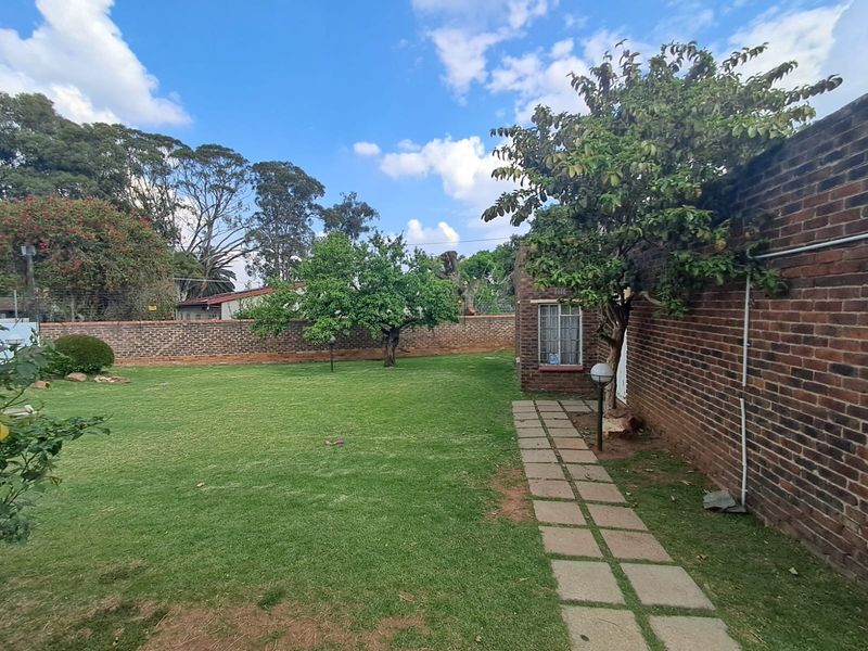 A spacious rear garden featuring a well-maintained lawn, brick boundary walls, and a paved walkway leading along the side of the house.