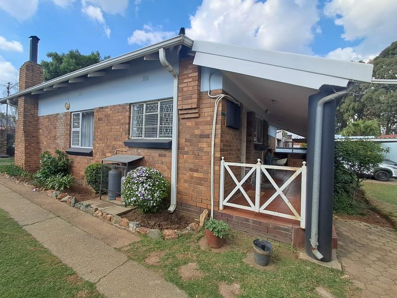 A side view of a brick house featuring a covered patio area, chimney, and paved walkway, showing standard residential exterior finishes.