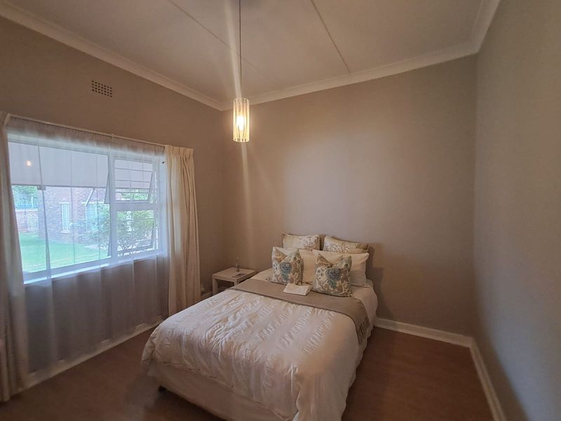 A well-maintained bedroom featuring neutral wall tones, laminate flooring, and a modern pendant light fixture, offering a clean and comfortable living space.