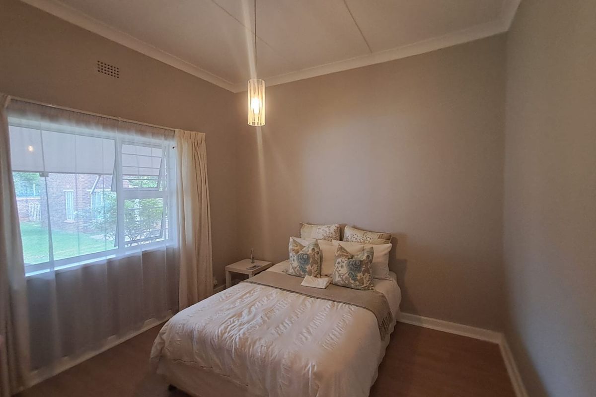 A well-maintained bedroom featuring neutral wall tones, laminate flooring, and a modern pendant light fixture, offering a clean and comfortable living space.