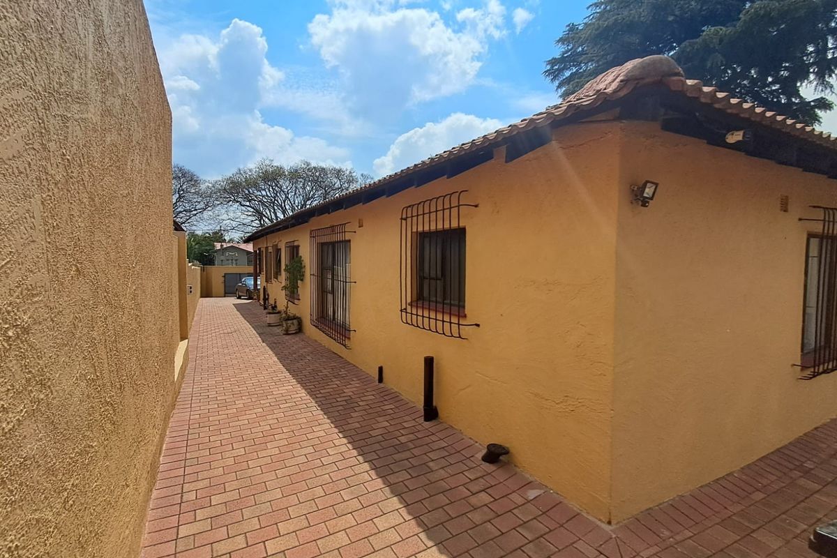 A side view of the property featuring a paved walkway, plastered exterior walls, security bars on windows, and a tiled roof.