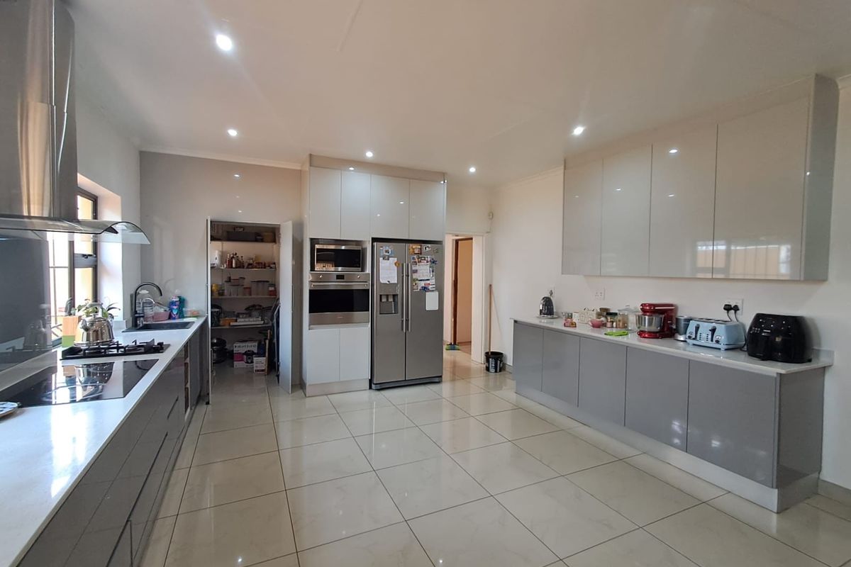 Modern kitchen featuring high-gloss cabinetry, stone countertops, integrated appliances, gas hob, and a spacious walk-in pantry with tiled flooring throughout.