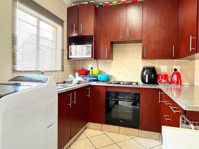 Compact kitchen featuring dark wood cabinetry, granite countertops, built-in oven, hob, and tiled finishes, providing a functional workspace with integrated laundry plumbing.