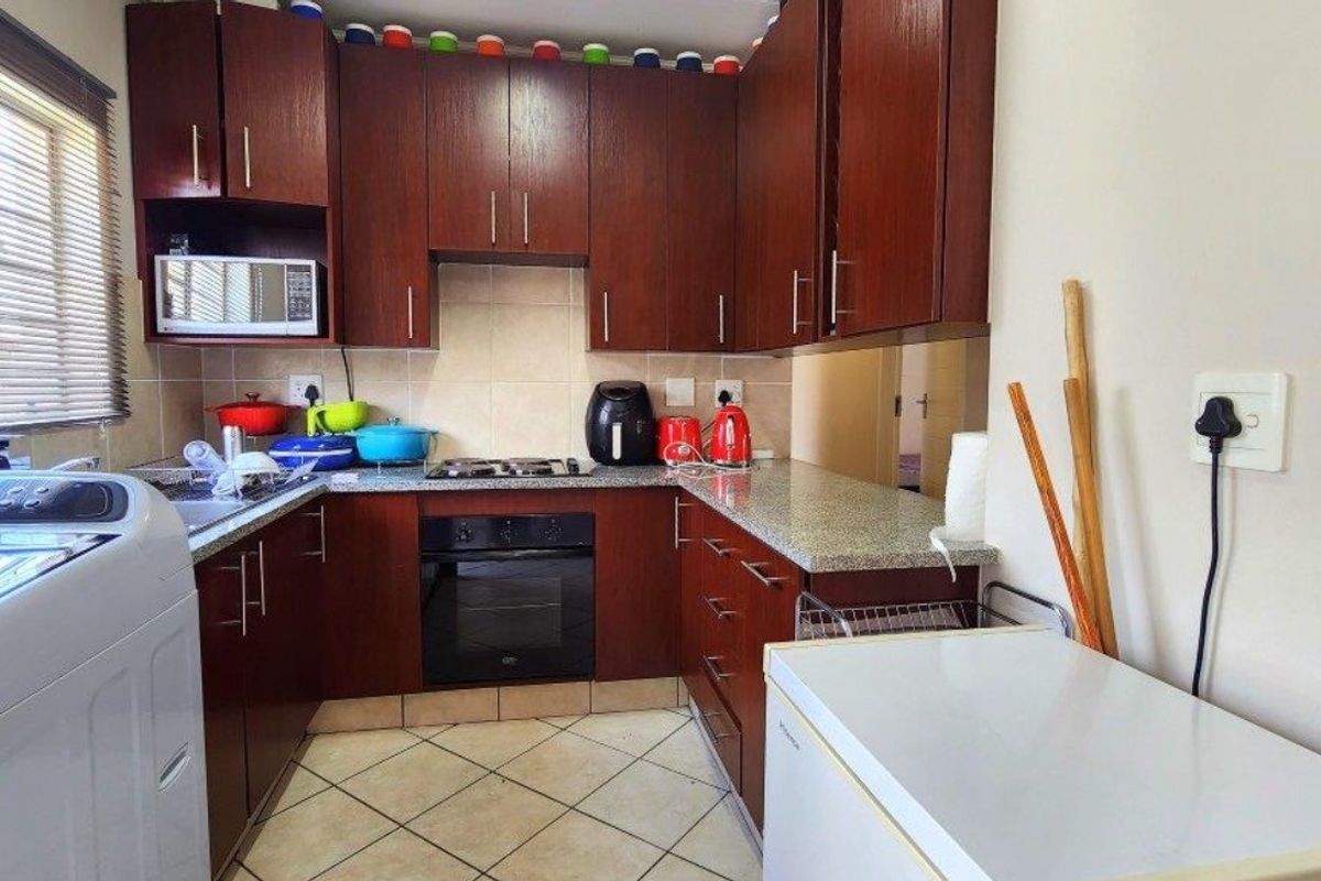 Compact kitchen featuring dark wood cabinetry, granite countertops, built-in oven, gas hob, and tiled flooring.