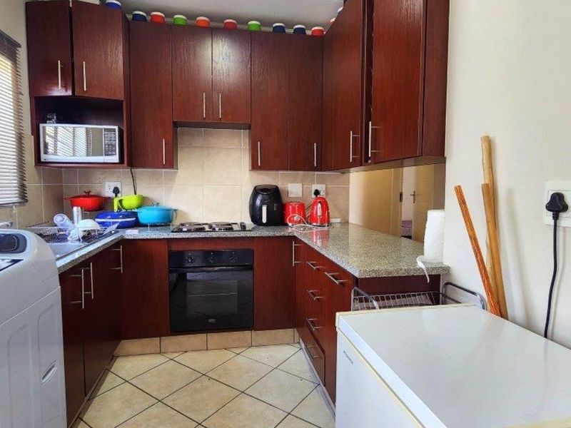 Compact kitchen featuring dark wood cabinetry, granite countertops, built-in oven, gas hob, and tiled flooring.
