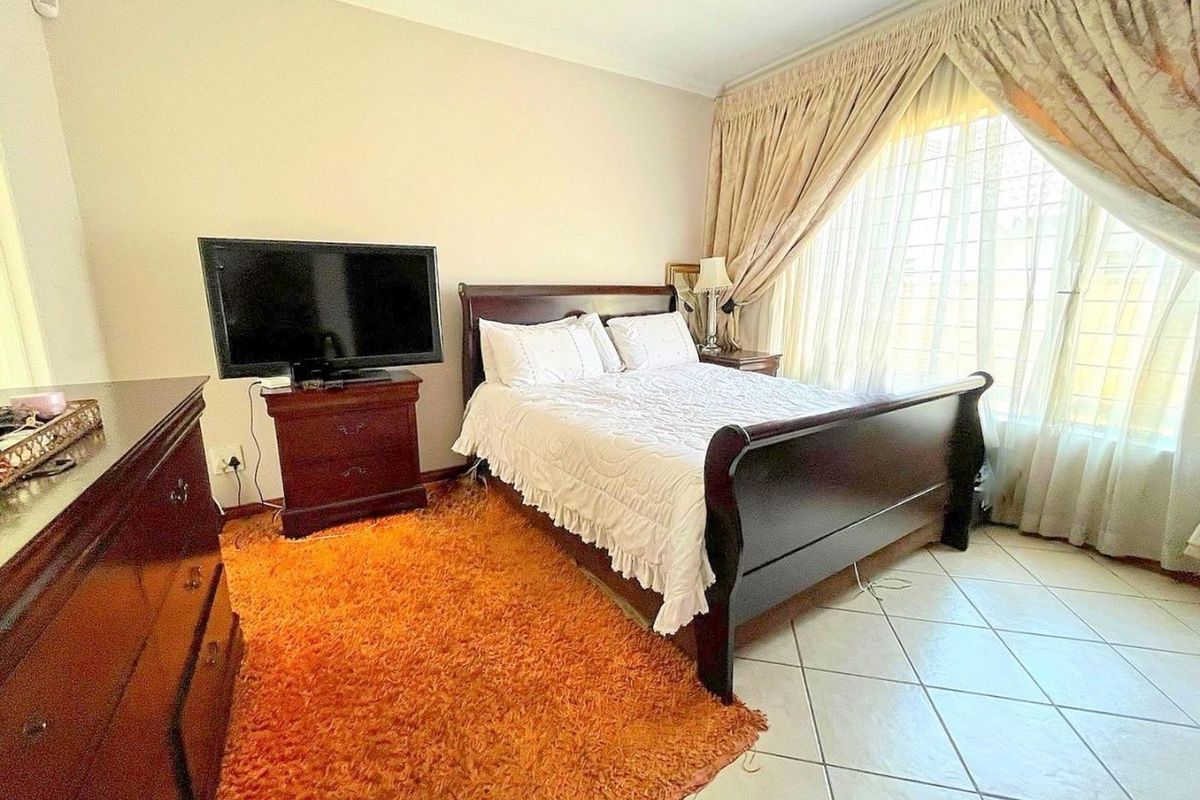 A well-lit bedroom featuring tiled flooring and large windows with security bars, offering a comfortable and functional living space.