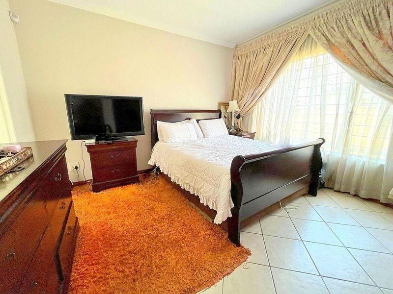 A well-lit bedroom featuring tiled flooring and large windows with security bars, offering a comfortable and functional living space.