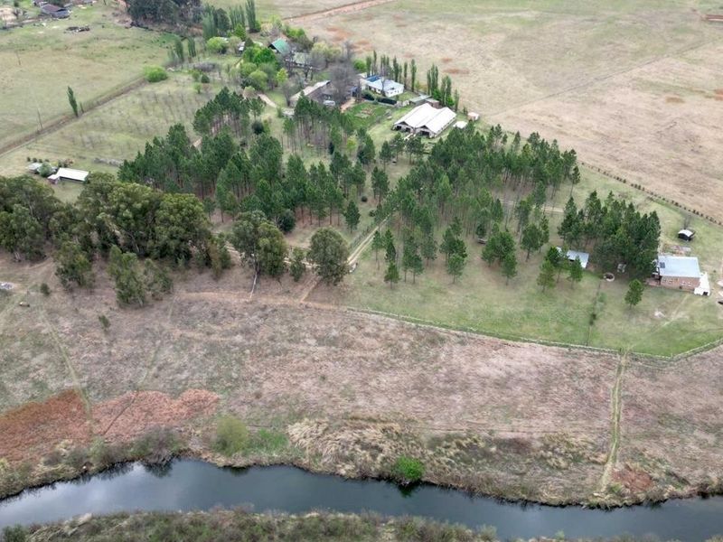 Aerial view of a large small holding property featuring extensive grounds, mature pine trees, multiple structures, and direct river frontage.