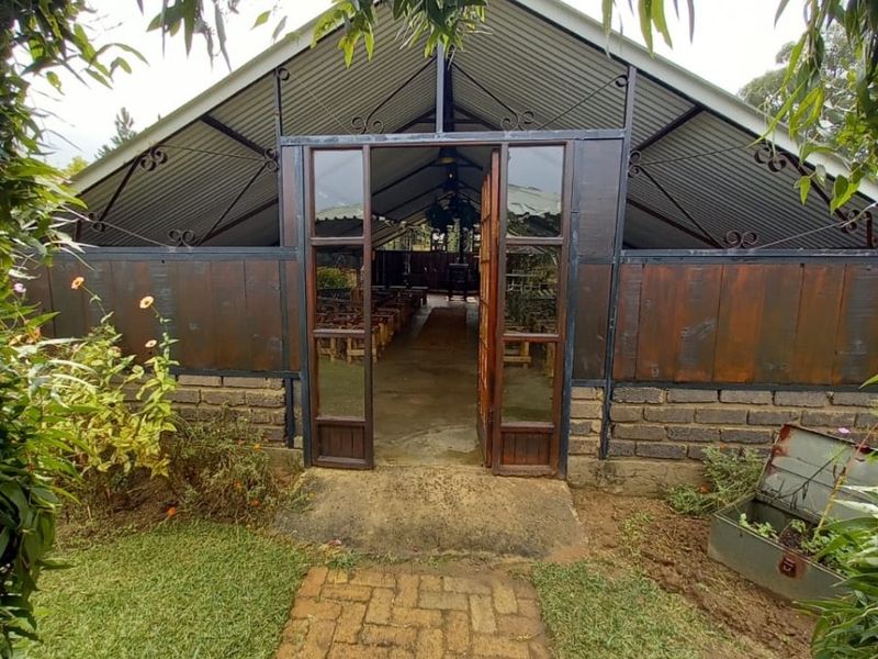 A rustic outdoor structure featuring a corrugated metal roof, brick base, and decorative wrought iron accents, accessed via a brick paved garden path.