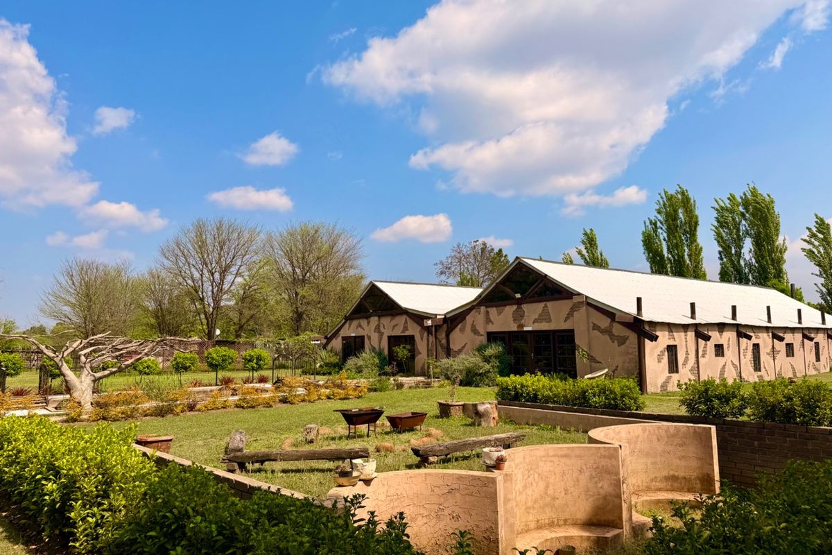 A view of the rear garden featuring a large barn-style building with a metal roof, landscaped grounds, and built-in masonry seating areas.