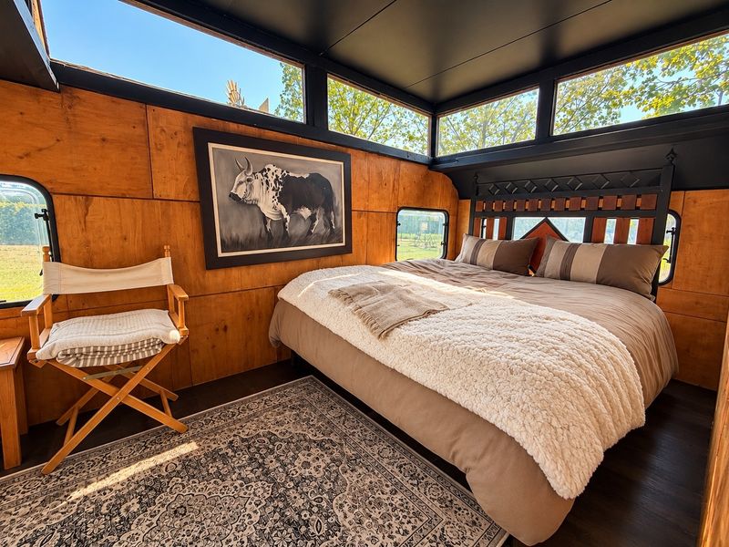 A cozy bedroom featuring warm plywood wall paneling, dark wood flooring, and expansive clerestory windows that provide ample natural light and scenic views.