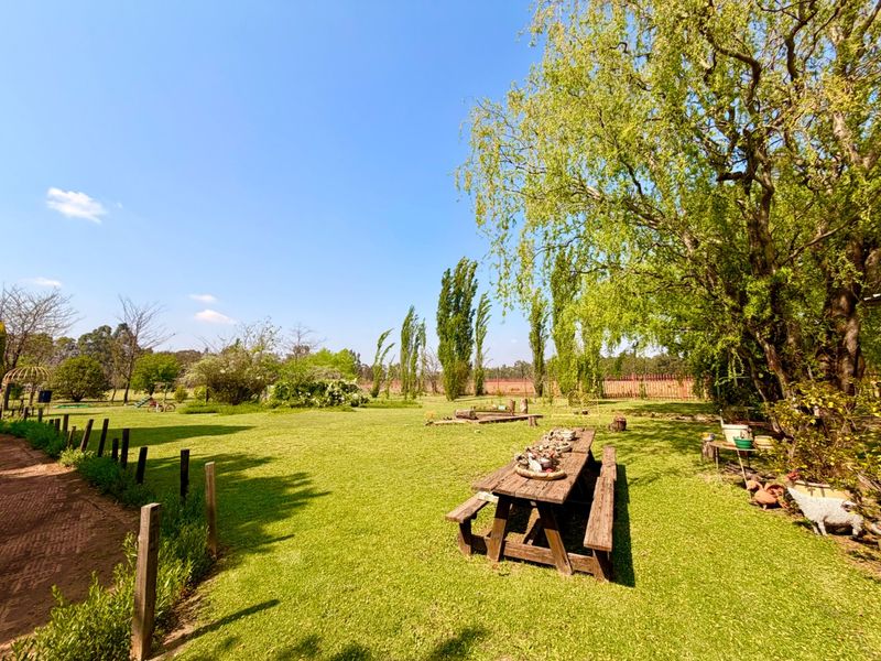 A spacious, well-maintained garden area featuring mature trees, expansive lawn, and a brick pathway, offering a peaceful outdoor setting.