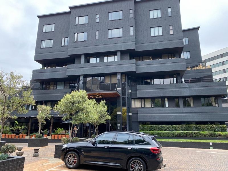 Modern multi-story apartment building featuring a dark brick facade, structured balconies, and a paved entrance area.