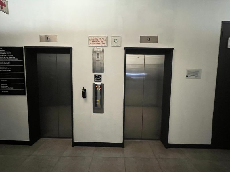 A clean and functional apartment building elevator lobby featuring dual stainless steel lift doors and clear building directory signage.