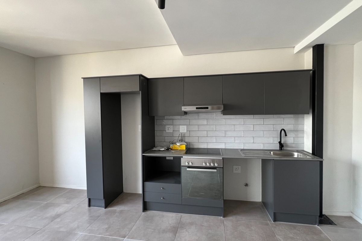 Modern kitchen featuring dark grey cabinetry, subway tile backsplash, integrated oven and hob, and tiled flooring in an open-plan layout.