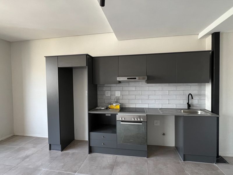 Modern kitchen featuring dark grey cabinetry, subway tile backsplash, integrated oven and hob, and tiled flooring in an open-plan layout.