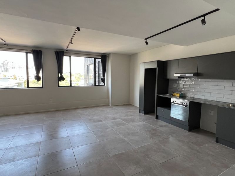 Spacious open-plan living area featuring modern dark cabinetry, integrated kitchen appliances, tiled flooring, and large windows providing ample natural light.