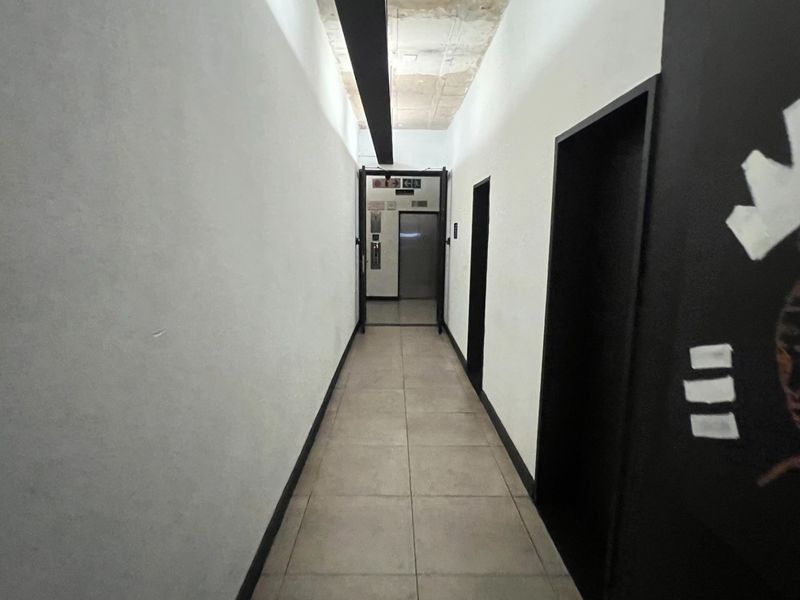 A functional apartment hallway featuring tiled flooring, exposed concrete ceiling details, and direct access to the building elevator.