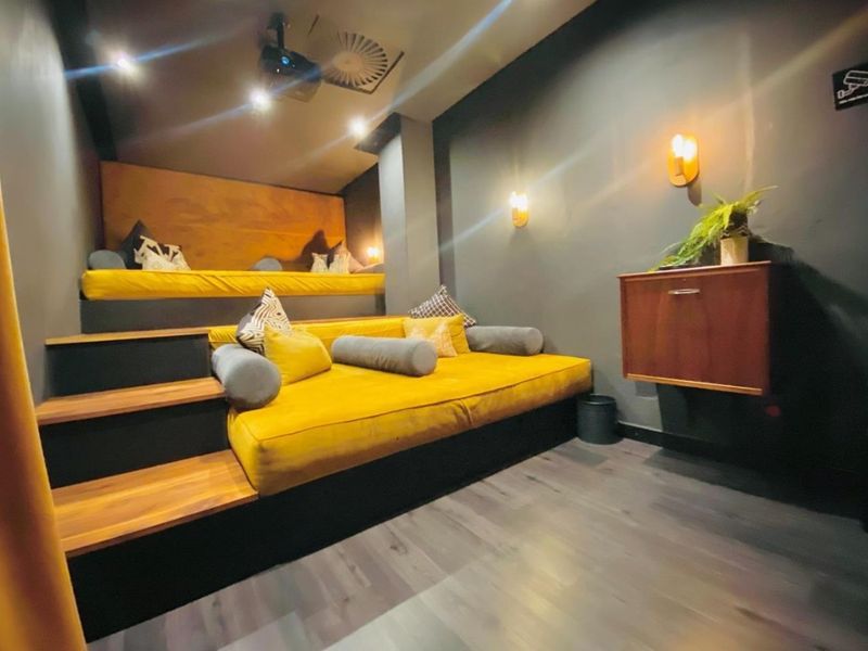 A dedicated cinema room featuring tiered seating platforms, integrated projector, and ambient wall lighting, finished with modern laminate flooring.
