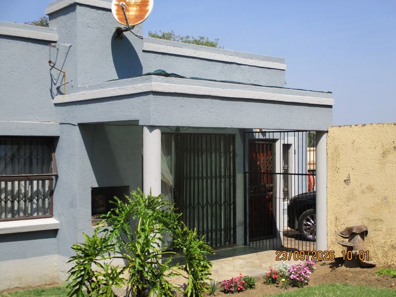 Front facade of a townhouse featuring a covered patio with a built-in braai, security gates, and tiled flooring.