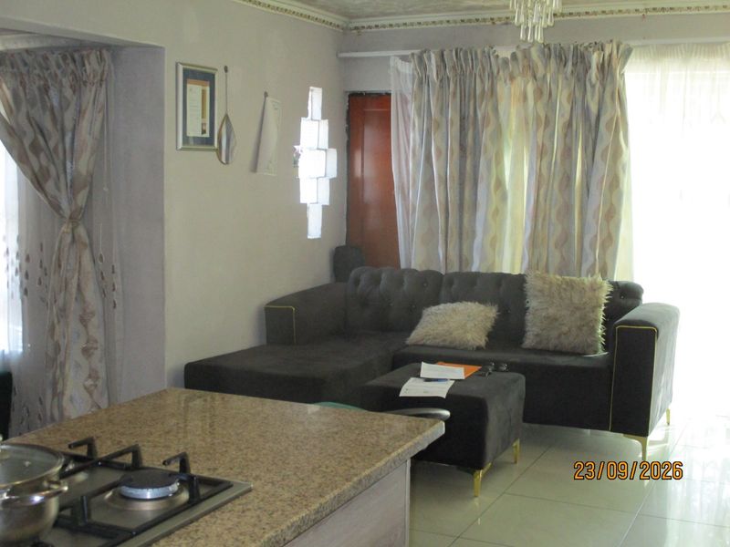 Open-plan living area featuring a kitchen island with a granite countertop and gas hob, flowing into a comfortable lounge space with tiled flooring.