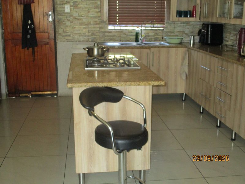 A functional kitchen featuring light wood-look cabinetry, granite countertops, a central island with a gas hob, and tiled flooring.