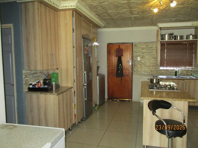 A functional kitchen featuring light wood cabinetry, granite countertops, a central island with a gas hob, and stone-cladding accents.