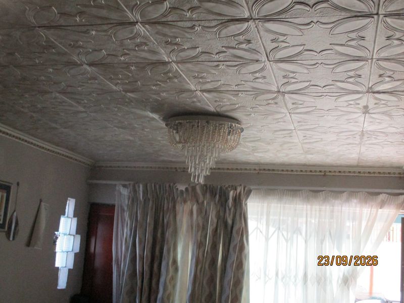 Living area featuring decorative ceiling tiles, crown molding, and a glass block window, illuminated by a central crystal chandelier.