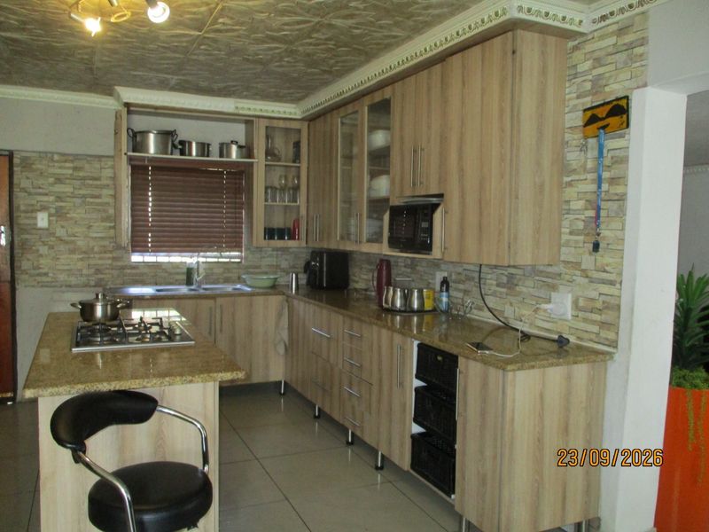 A functional kitchen featuring light wood-finish cabinetry, granite countertops, a gas hob, and stone-cladding wall accents with tiled flooring.