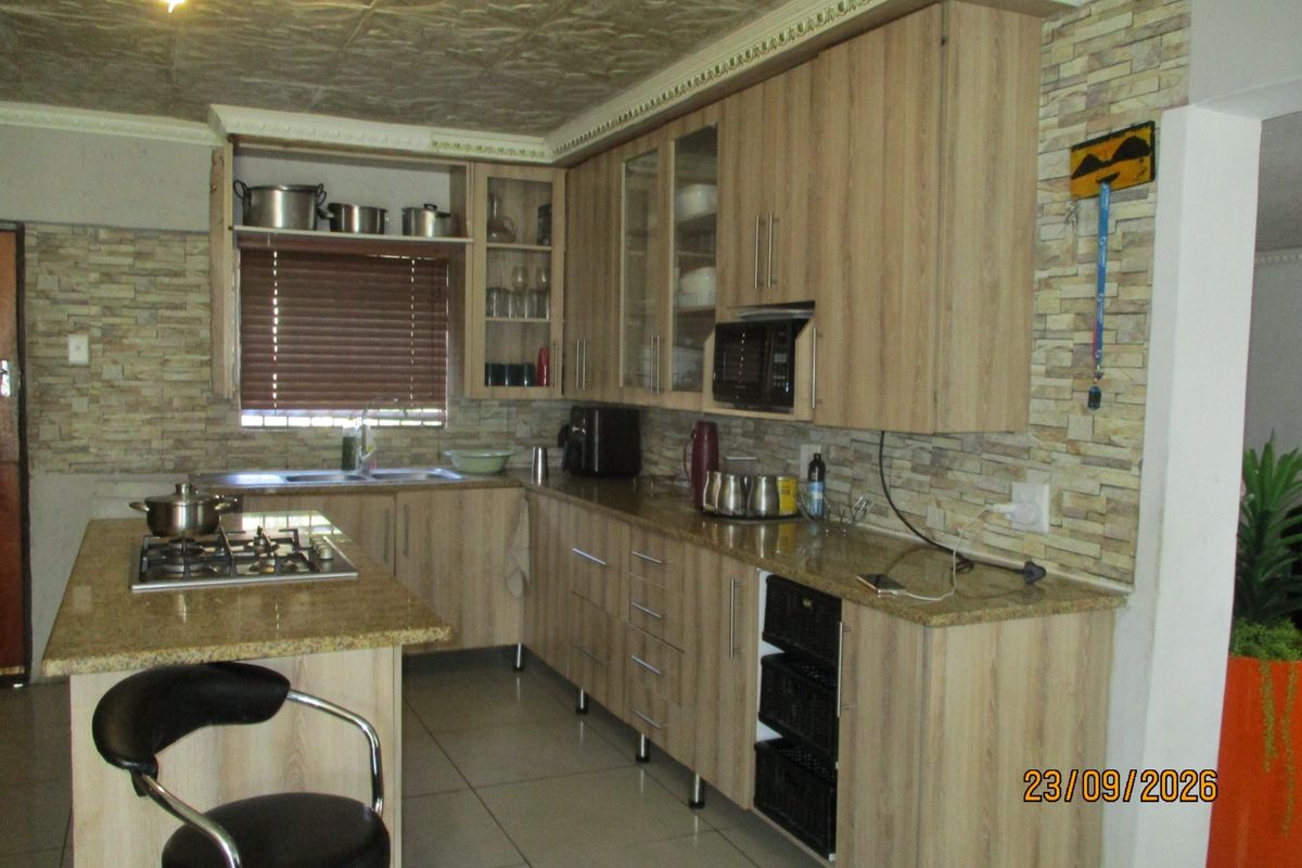 A functional kitchen featuring light wood-finish cabinetry, granite countertops, a gas hob, and stone-cladding wall accents with tiled flooring.