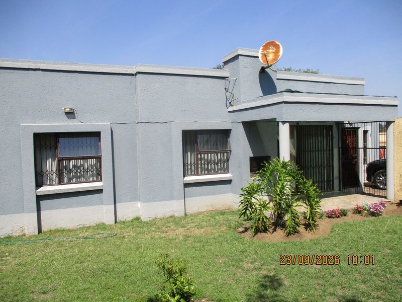 Front elevation of a townhouse featuring a covered entrance, security gates, burglar bars, and a small front garden area.