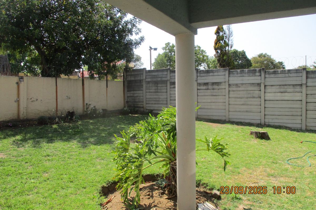 A view of the rear garden and lawn area from a covered patio, featuring a concrete boundary wall.