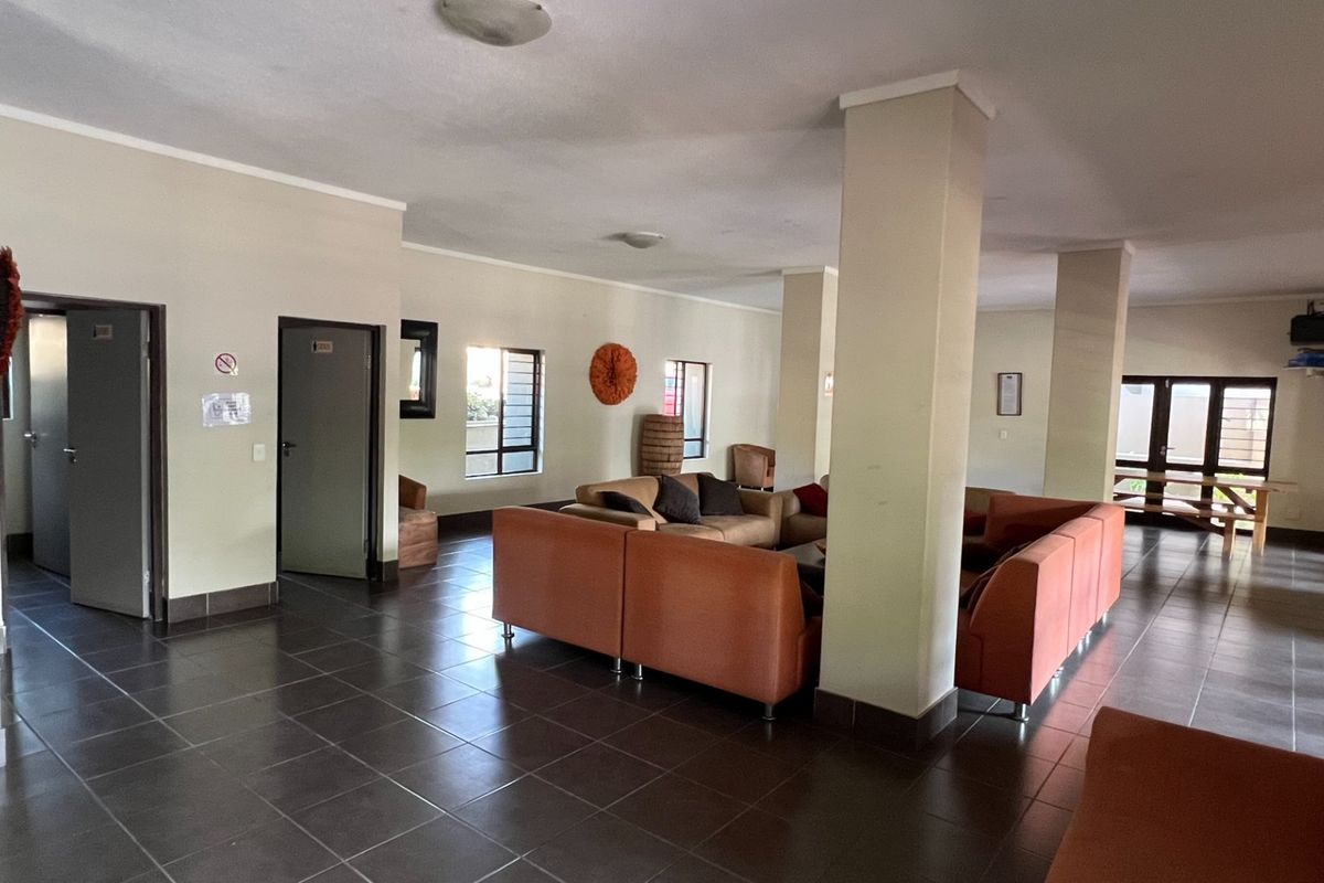 Spacious open-plan living area featuring dark tiled flooring, structural support columns, and multiple windows providing natural light.