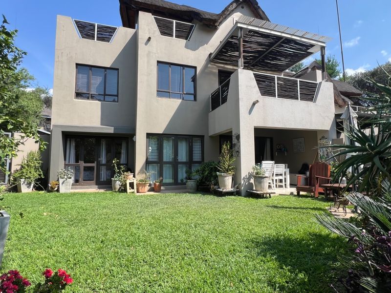 Rear view of a multi-story apartment featuring a landscaped garden, a covered balcony with timber pergola, and large sliding glass doors.