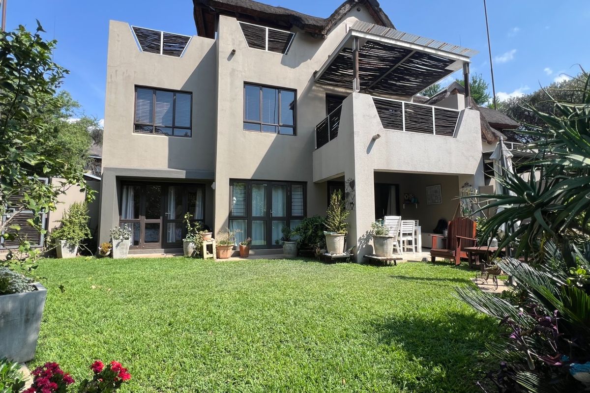 Rear view of a multi-story apartment featuring a landscaped garden, a covered balcony with timber pergola, and large sliding glass doors.