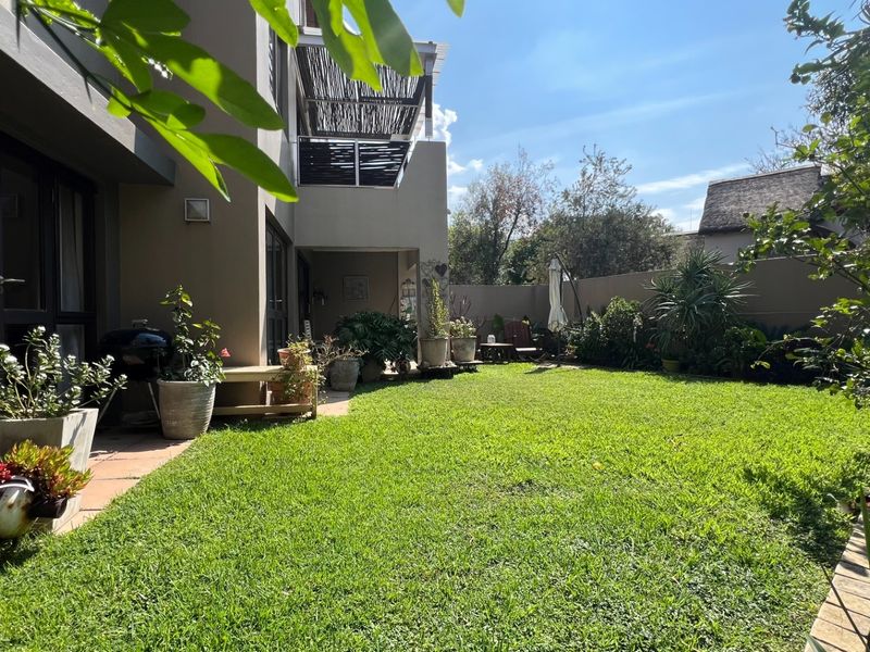 A well-maintained rear garden featuring a lush lawn, paved walkway, and a covered patio area attached to the apartment building.