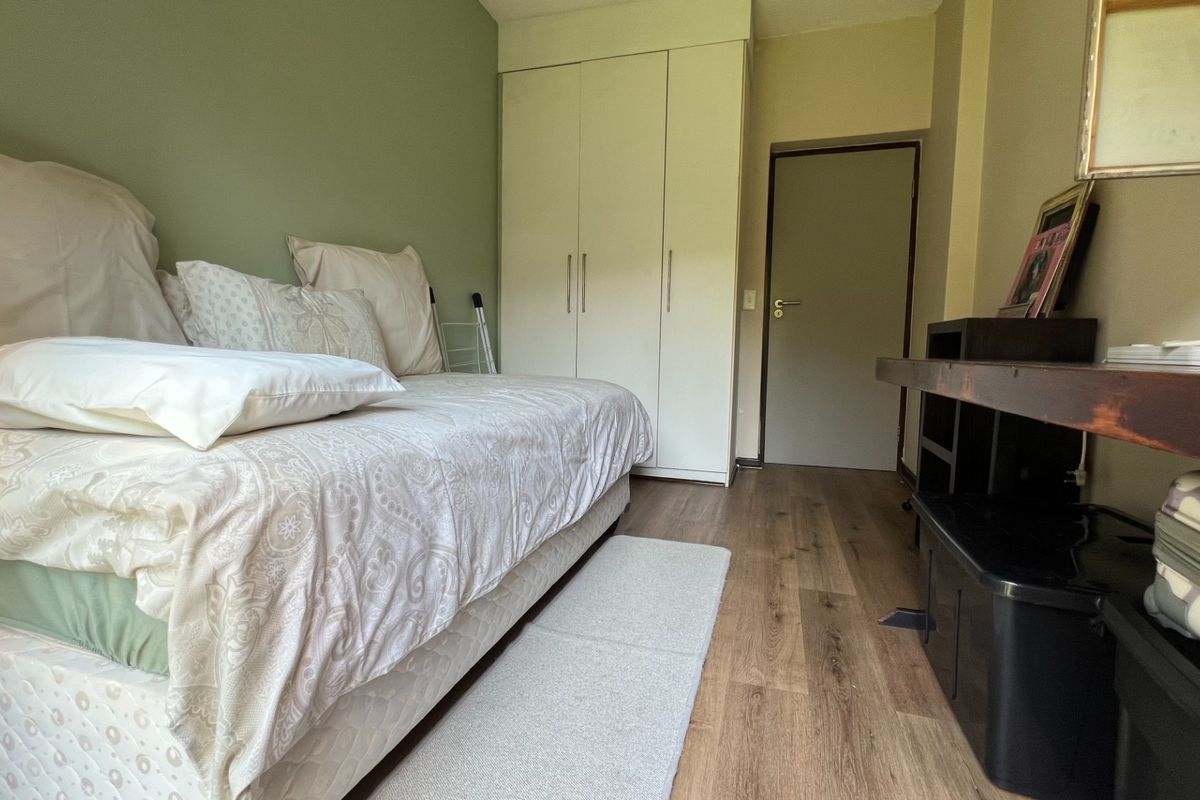 A functional bedroom featuring laminate flooring and a built-in wardrobe with neutral wall finishes.