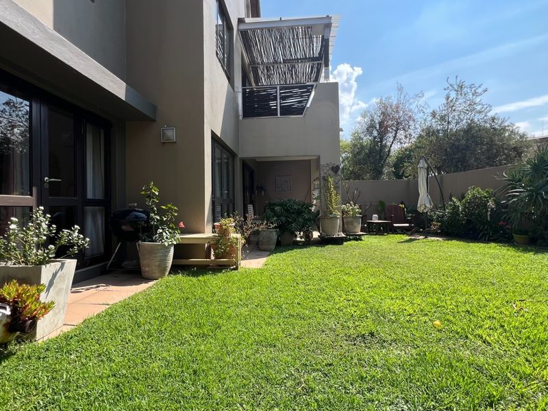 A private rear garden featuring a well-maintained lawn, paved patio area, and a balcony with a pergola overhead.