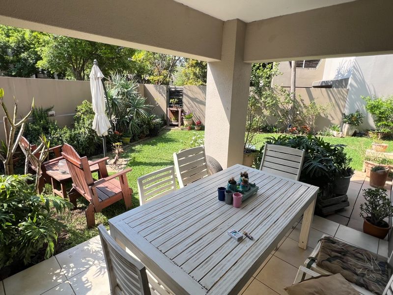 A covered patio area featuring tiled flooring and a concrete support pillar, overlooking a private garden space with boundary walls.