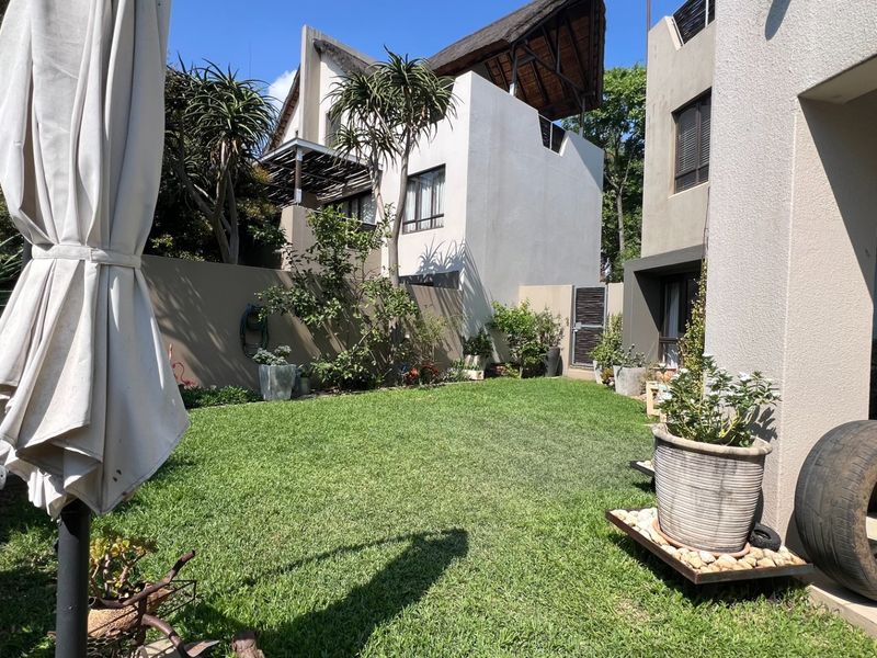 A well-maintained private rear garden featuring a lush lawn, boundary walls, and a paved patio area adjacent to the apartment building.