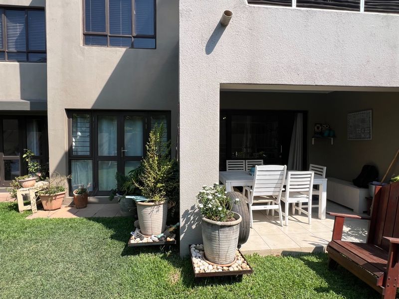 A rear view of the apartment featuring a covered patio area with tiled flooring, leading out onto a private garden space.