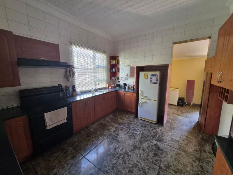 A functional kitchen featuring wooden cabinetry, a built-in stove with extractor fan, tiled splashbacks, and durable tiled flooring.