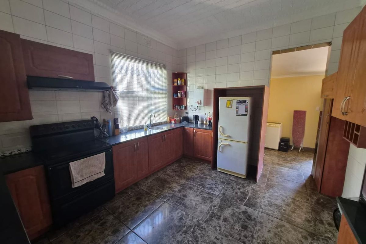 A functional kitchen featuring wooden cabinetry, a built-in stove with extractor fan, tiled splashbacks, and durable tiled flooring.