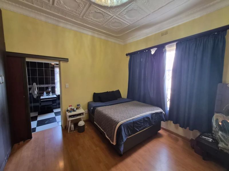A bedroom featuring laminate flooring and a decorative pressed metal ceiling, with direct access to an en-suite bathroom.